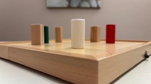 Aufstellungsbrett mit farbigen Holzfiguren zur Darstellung von Systemen in der systemischen Aufstellungsarbeit. Das Bild veranschaulicht die Konfliktlösung mit systemischer Aufstellung durch die Visualisierung von Dynamiken und Beziehungen in Konfliktlösungsprozessen, Coaching und Mediation.