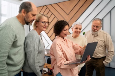 Das Bild zeigt ein Team aus älteren und jüngeren Mitarbeitenden, die gemeinsam und offensichtlichem Spaß an einem Laptop arbeiten. Es symbolisiert: Generationenmix im Unternehmen als Erfolgsfaktor 