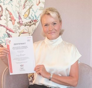 Beate Reinhart: sie zeigt ihr Zertifikat von TÜV AUSTRIA: Personenzertifizierung als Wertorientierter systemischer Coach und Berater, ISO/IEC 17024