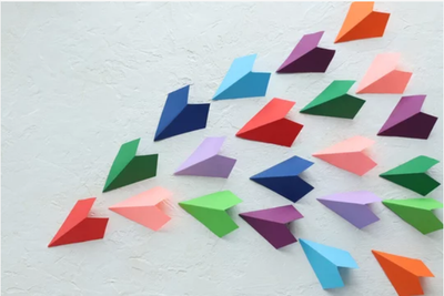 Bunte Papierflieger in geordneter Formation als Symbol für Teamführung, Zusammenarbeit und Führungskompetenz stärken.