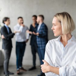 Eine Frau steht isoliert vor einer Gruppe von Kolleg:innen. Das Bild veranschaulicht Mobbing am Arbeitsplatz.