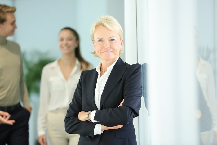 Beate Reinhart, Business-Coach und Mediatorin mit zwei zufriedenen Klienten im Hintergrund. Das Bild steht für die Referenzen & Erfahrungen von Klient:innen mit Mediation & Business Coaching bei Kompetenz Mensch.