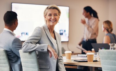 Zufrieden lächelnde weibliche Führungskraft in einer Besprechungssituation – symbolisiert die Unterstützung durch Coaching für Führungskräfte bei der Entwicklung von Führungskompetenzen und Teamdynamik.